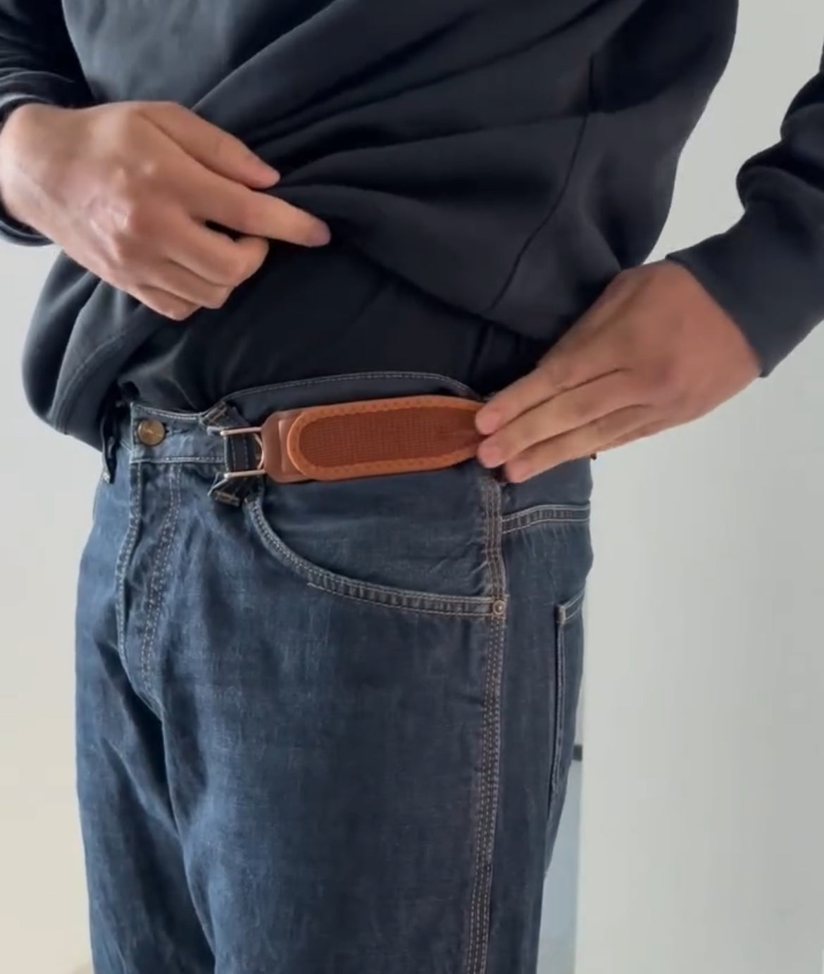 Person wearing blue jeans with a brown leather belt on a plain background