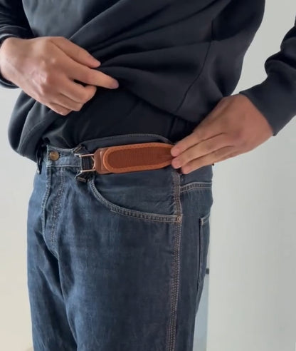 Person wearing blue jeans with a brown leather belt on a plain background